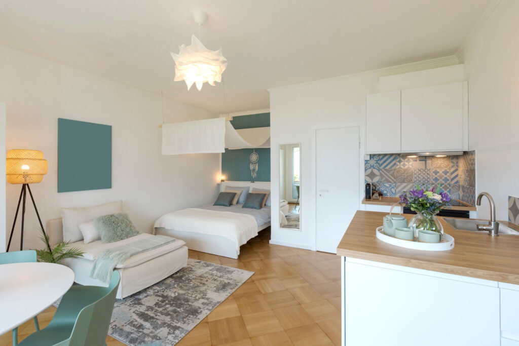 Helles, modern eingerichtetes Micro-Apartment mit Doppelbett, gemütlicher Sitzecke, Essbereich und offener Küche.
